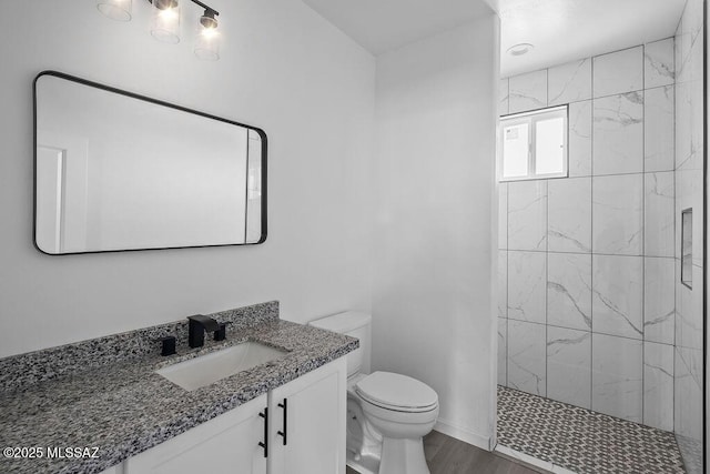 bathroom with a tile shower, vanity, toilet, and wood-type flooring