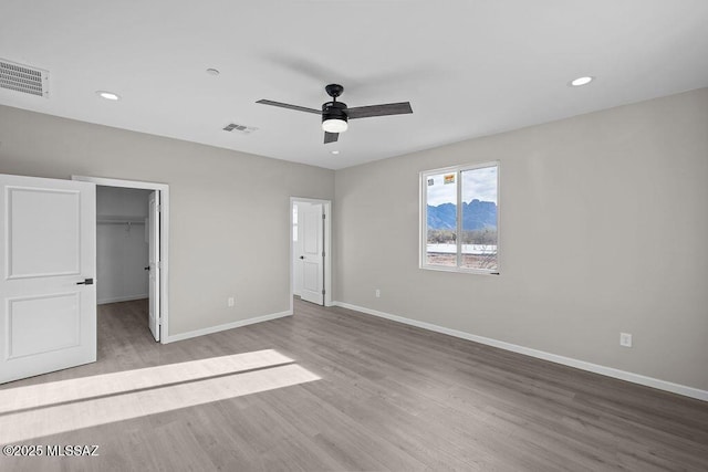 unfurnished bedroom featuring a spacious closet, a closet, ceiling fan, and light wood-type flooring