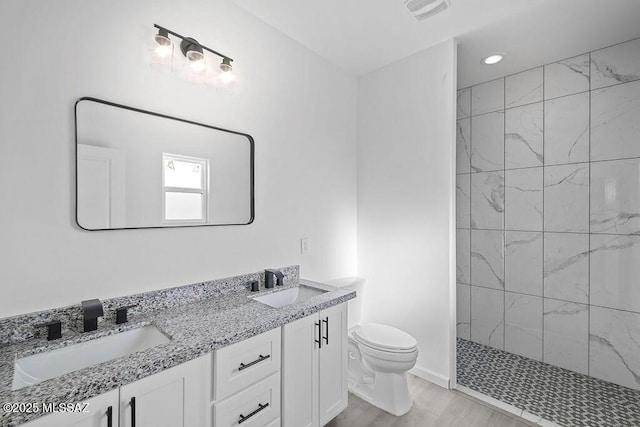 bathroom featuring vanity, toilet, wood-type flooring, and a tile shower