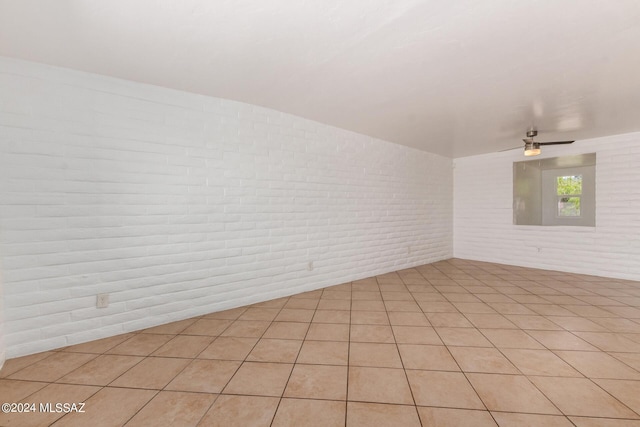 tiled empty room featuring ceiling fan and brick wall