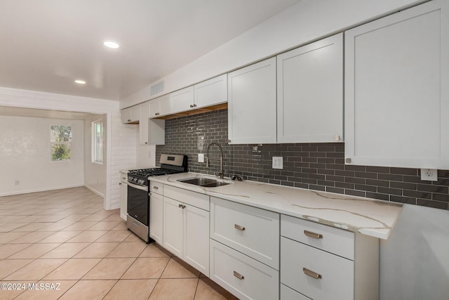 kitchen with light stone counters, gas range, sink, white cabinetry, and light tile patterned flooring