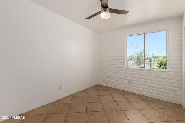 tiled spare room with ceiling fan and brick wall