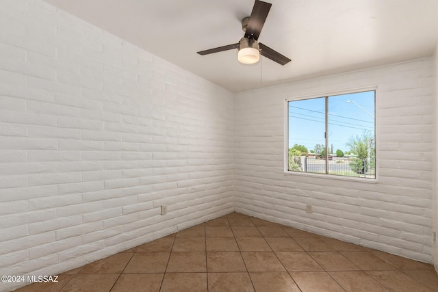 tiled empty room with ceiling fan and brick wall