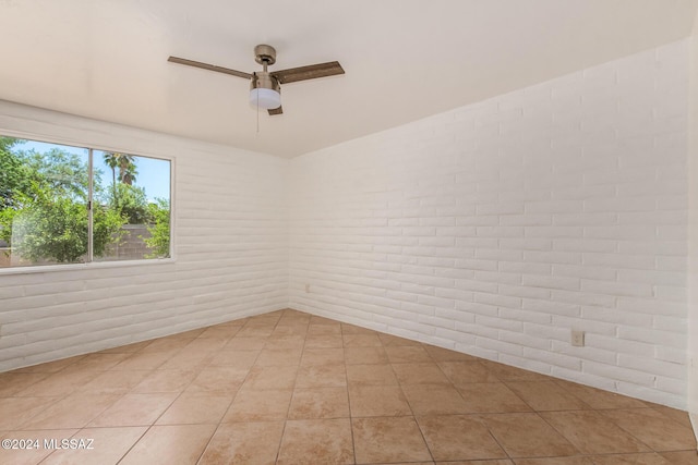 spare room featuring ceiling fan, light tile patterned flooring, and brick wall