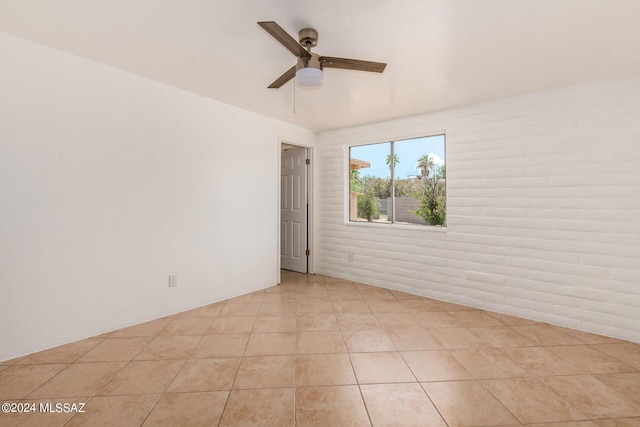 tiled empty room featuring ceiling fan and brick wall