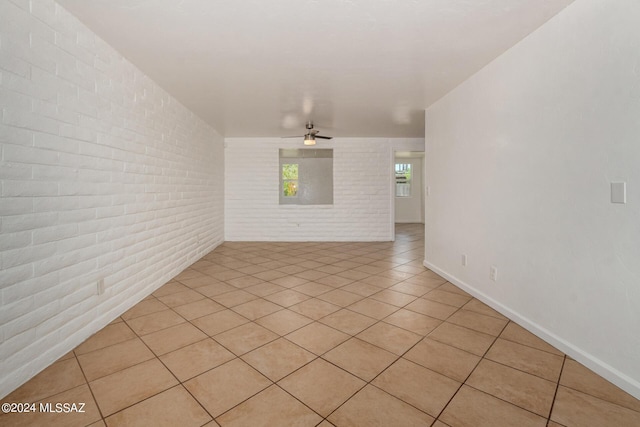 unfurnished room with light tile patterned flooring, ceiling fan, and brick wall