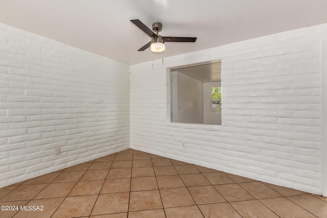 tiled empty room with ceiling fan and brick wall