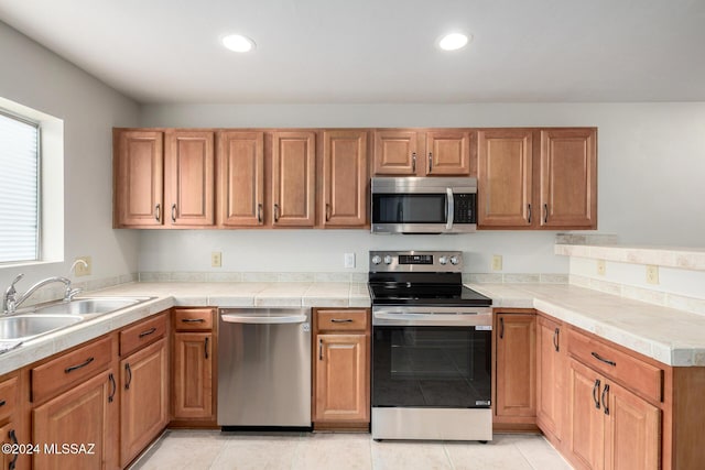 kitchen with appliances with stainless steel finishes, light tile patterned floors, tile counters, and sink