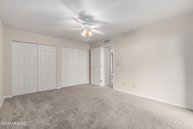 unfurnished bedroom featuring carpet floors, ceiling fan, and multiple closets