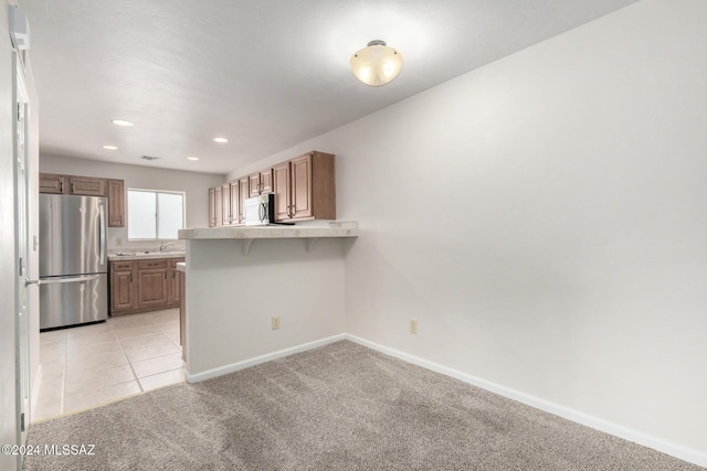 kitchen featuring kitchen peninsula, a kitchen breakfast bar, stainless steel appliances, light colored carpet, and sink