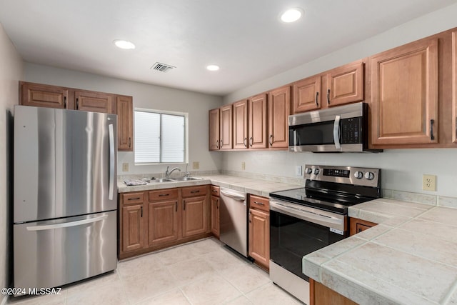 kitchen with light tile patterned floors, stainless steel appliances, tile counters, and sink