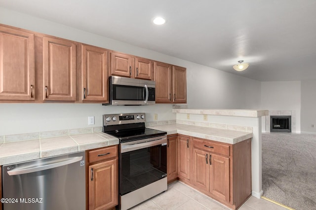 kitchen featuring light colored carpet, stainless steel appliances, and a tile fireplace