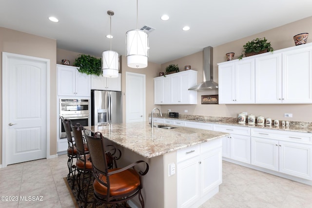 kitchen featuring sink, wall chimney range hood, an island with sink, white cabinets, and appliances with stainless steel finishes