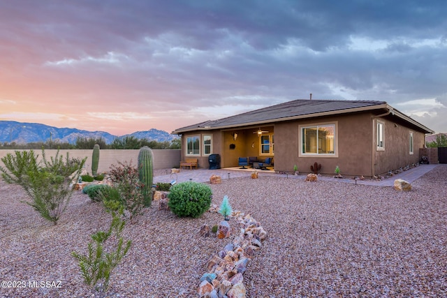 back house at dusk featuring a mountain view and a patio