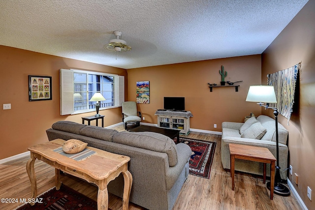 living room featuring ceiling fan, light wood-type flooring, and a textured ceiling