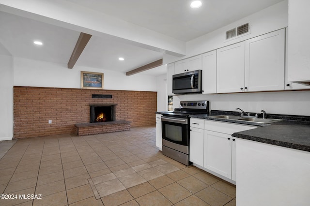 kitchen featuring white cabinets, appliances with stainless steel finishes, light tile patterned floors, and beamed ceiling