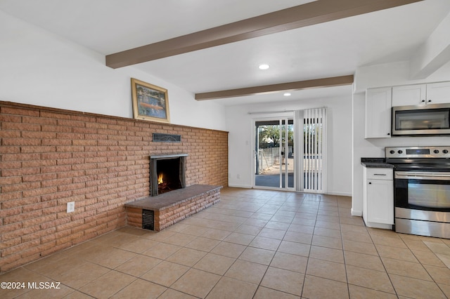 kitchen with white cabinetry, beamed ceiling, brick wall, light tile patterned flooring, and appliances with stainless steel finishes