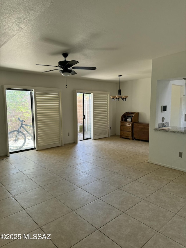 tiled empty room with plenty of natural light and ceiling fan with notable chandelier