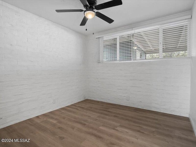 unfurnished room with ceiling fan, hardwood / wood-style floors, and brick wall