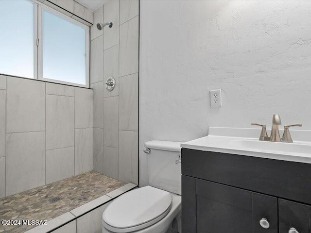 bathroom with a tile shower, vanity, and toilet