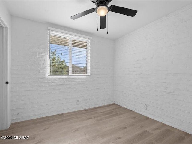 empty room with ceiling fan, light hardwood / wood-style flooring, and brick wall