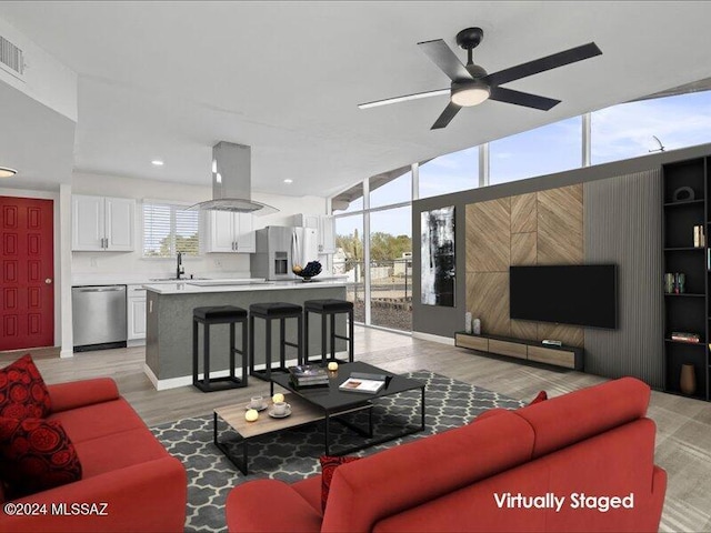 living room with floor to ceiling windows, ceiling fan, sink, and light hardwood / wood-style floors