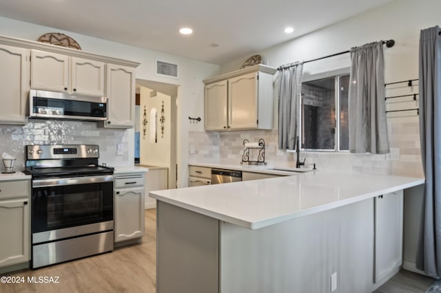 kitchen featuring decorative backsplash, light hardwood / wood-style floors, kitchen peninsula, and stainless steel appliances