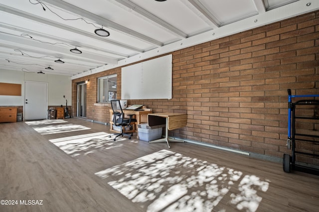 interior space with beam ceiling, hardwood / wood-style flooring, and brick wall