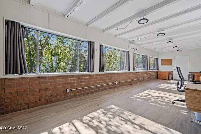 interior space featuring a wall unit AC, light hardwood / wood-style flooring, beamed ceiling, and brick wall