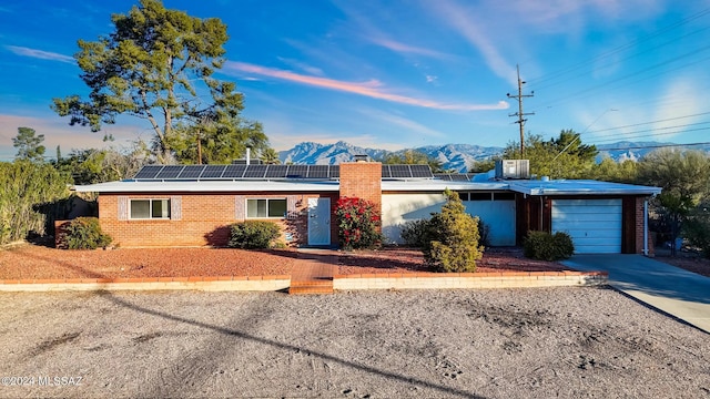 ranch-style home with solar panels, a garage, and a mountain view