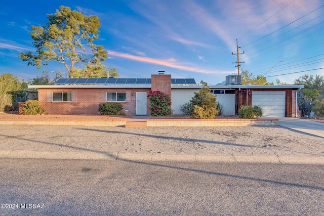 ranch-style home with central air condition unit, a garage, and solar panels