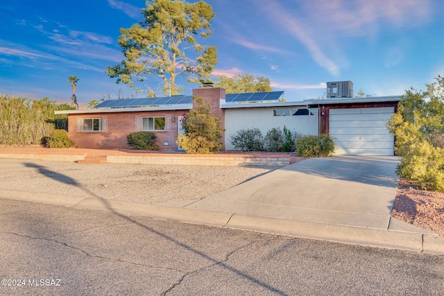 ranch-style house with solar panels, cooling unit, and a garage