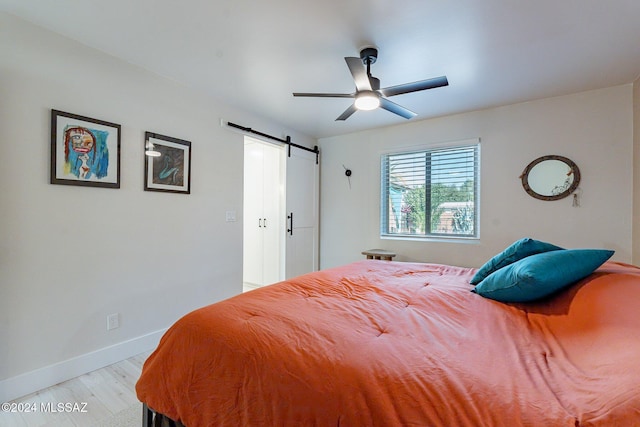 bedroom featuring a barn door, ceiling fan, and light hardwood / wood-style floors