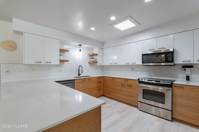 kitchen featuring sink, light wood-type flooring, appliances with stainless steel finishes, tasteful backsplash, and white cabinetry