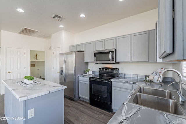 kitchen featuring dark wood-type flooring, sink, light stone countertops, appliances with stainless steel finishes, and a kitchen island