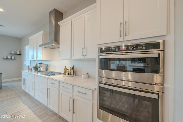 kitchen featuring appliances with stainless steel finishes, tasteful backsplash, white cabinetry, and wall chimney range hood