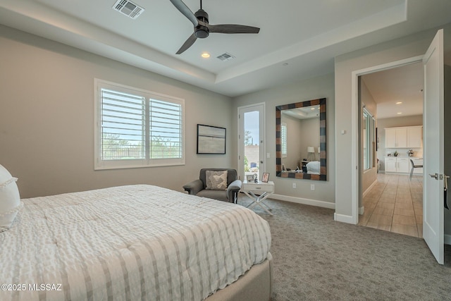 bedroom featuring multiple windows, light colored carpet, a raised ceiling, and ceiling fan