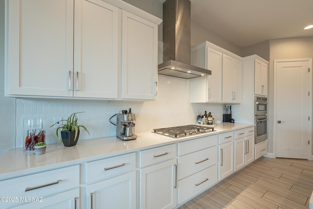 kitchen with stainless steel appliances, white cabinetry, tasteful backsplash, and wall chimney range hood