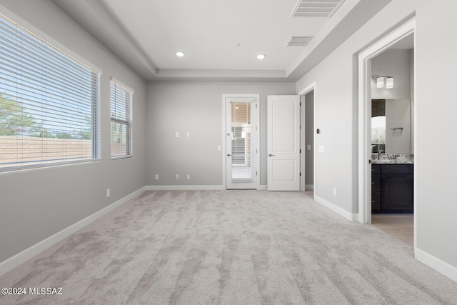 unfurnished bedroom with a raised ceiling, ensuite bath, and light carpet