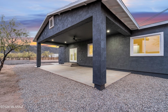 property exterior at dusk featuring ceiling fan and a patio