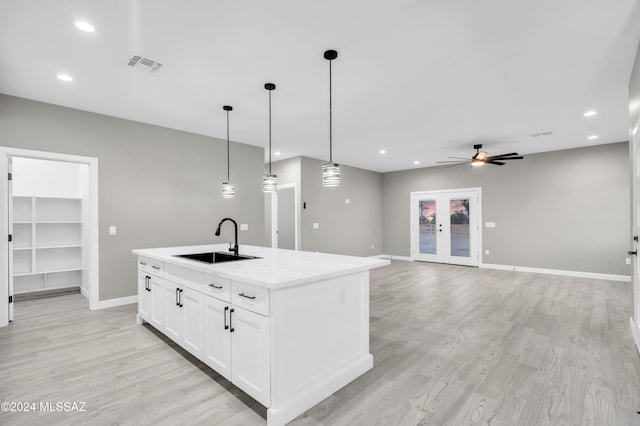 kitchen featuring pendant lighting, a kitchen island with sink, white cabinets, sink, and light wood-type flooring