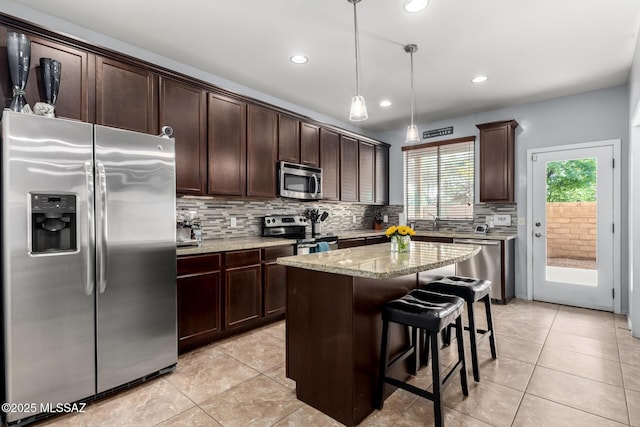 kitchen with a center island, a kitchen bar, appliances with stainless steel finishes, decorative light fixtures, and light stone counters