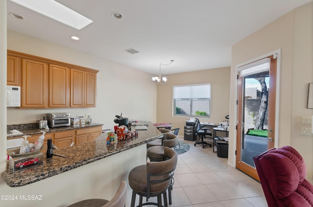 kitchen with a skylight, light tile patterned floors, an inviting chandelier, dark stone countertops, and hanging light fixtures