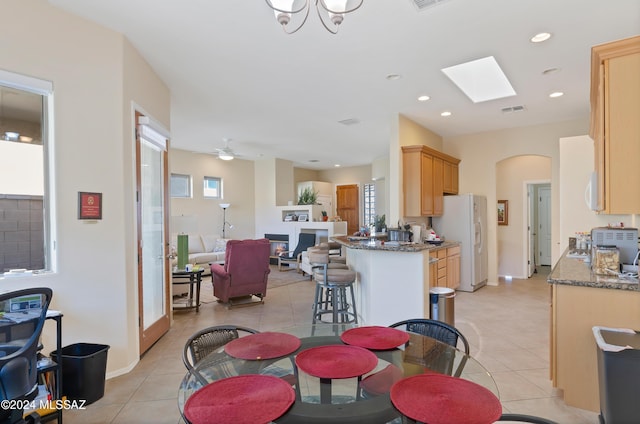 kitchen with light brown cabinets, ceiling fan with notable chandelier, dark stone countertops, white fridge with ice dispenser, and kitchen peninsula