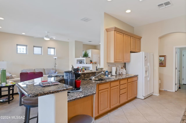 kitchen featuring dark stone counters, sink, ceiling fan, white fridge with ice dispenser, and kitchen peninsula