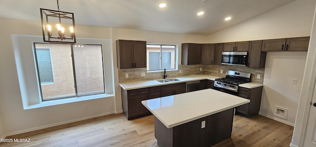 kitchen featuring a center island, sink, vaulted ceiling, appliances with stainless steel finishes, and decorative light fixtures