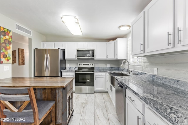 kitchen featuring sink, dark stone countertops, tasteful backsplash, white cabinetry, and stainless steel appliances