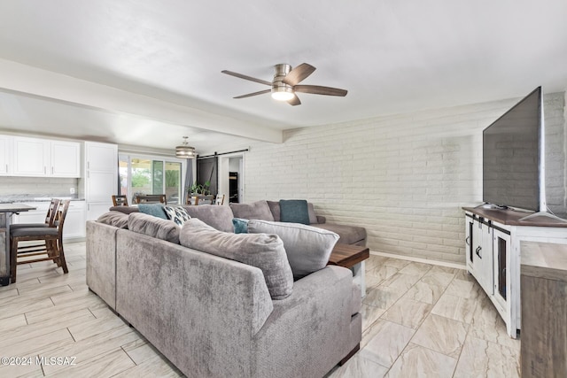 living room featuring a barn door, ceiling fan, beamed ceiling, and brick wall