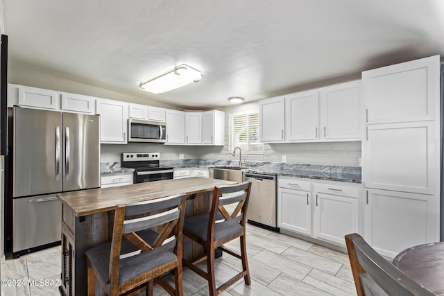 kitchen featuring white cabinets, stainless steel appliances, and dark stone counters