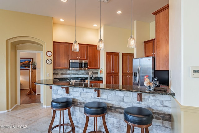 kitchen featuring stainless steel appliances, dark stone countertops, kitchen peninsula, decorative light fixtures, and a breakfast bar area